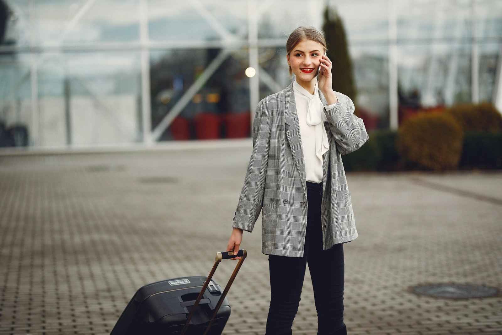 Confident businesswoman walking with luggage while talking on phone at airport terminal.